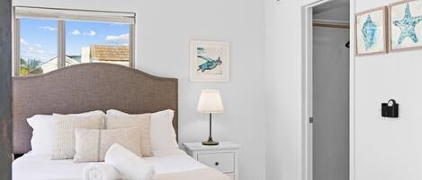 A neatly made bed with a headboard, a bedside lamp, and a window with blinds.