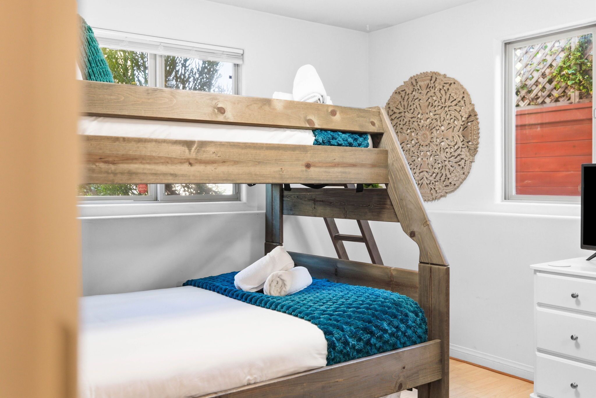 Un lit superposé avec une échelle en bois, du linge de lit blanc et une couverture bleue.