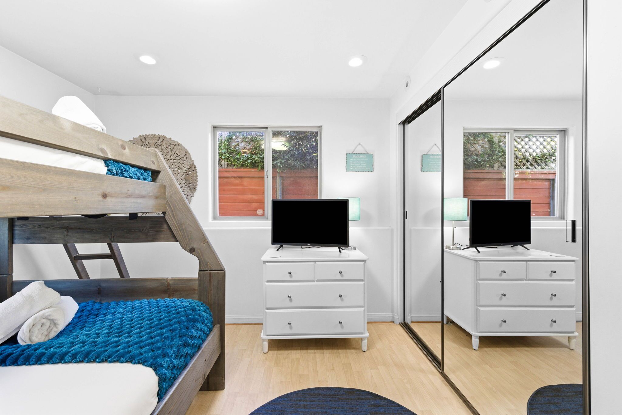 A bedroom with a bunk bed, a white dresser, a flat-screen TV, and a large mirror.