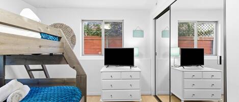 A bedroom with a bunk bed, a white dresser, a flat-screen TV, and a large mirror.