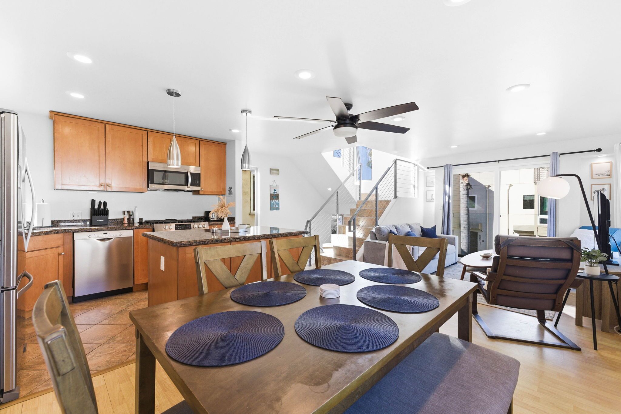 A modern kitchen with wooden cabinets, stainless steel appliances, and a dining area with a wooden table and blue placemats.