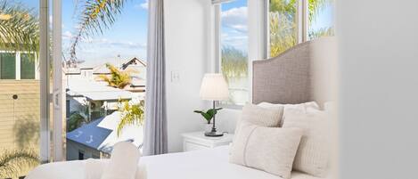 A modern hotel room with a large bed, a bedside table with a lamp, and a view of the outside.