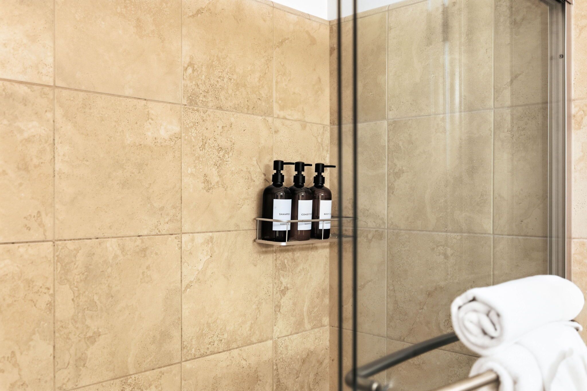 A bathroom with beige tiles, a glass shower enclosure, and a towel rack with a rolled towel.