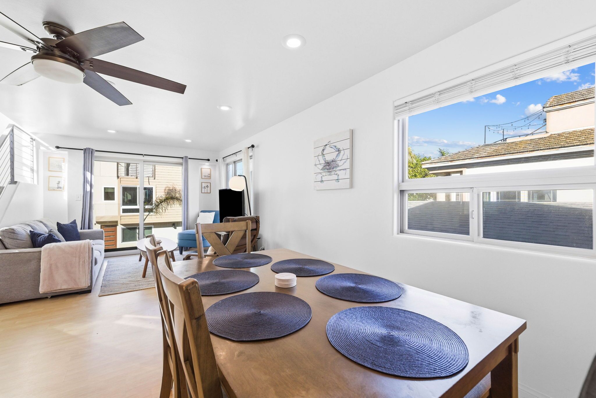 A modern dining area with a wooden table, blue placemats, and a ceiling fan.