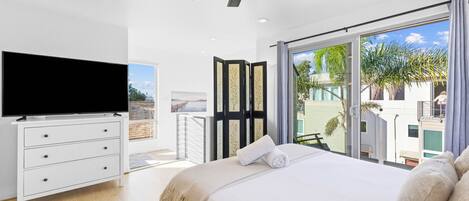 Ein modernes Schlafzimmer mit Flachbildfernseher, Deckenventilator, einem großen Bett mit Ausblick und einer Glasschiebetür, die auf einen Balkon führt.