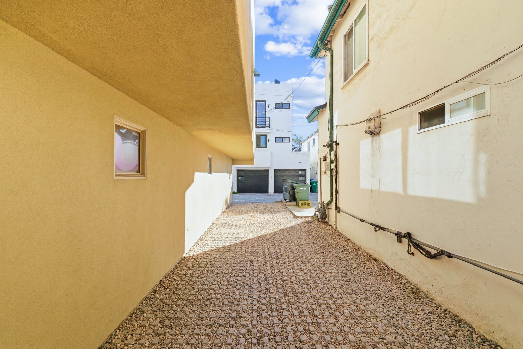 Une ruelle étroite, au sol pavé, bordée de bâtiments aux murs et aux fenêtres de couleur claire.
