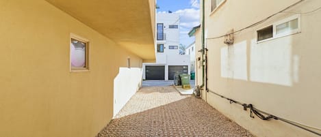 Une ruelle étroite, au sol pavé, bordée de bâtiments aux murs et aux fenêtres de couleur claire.