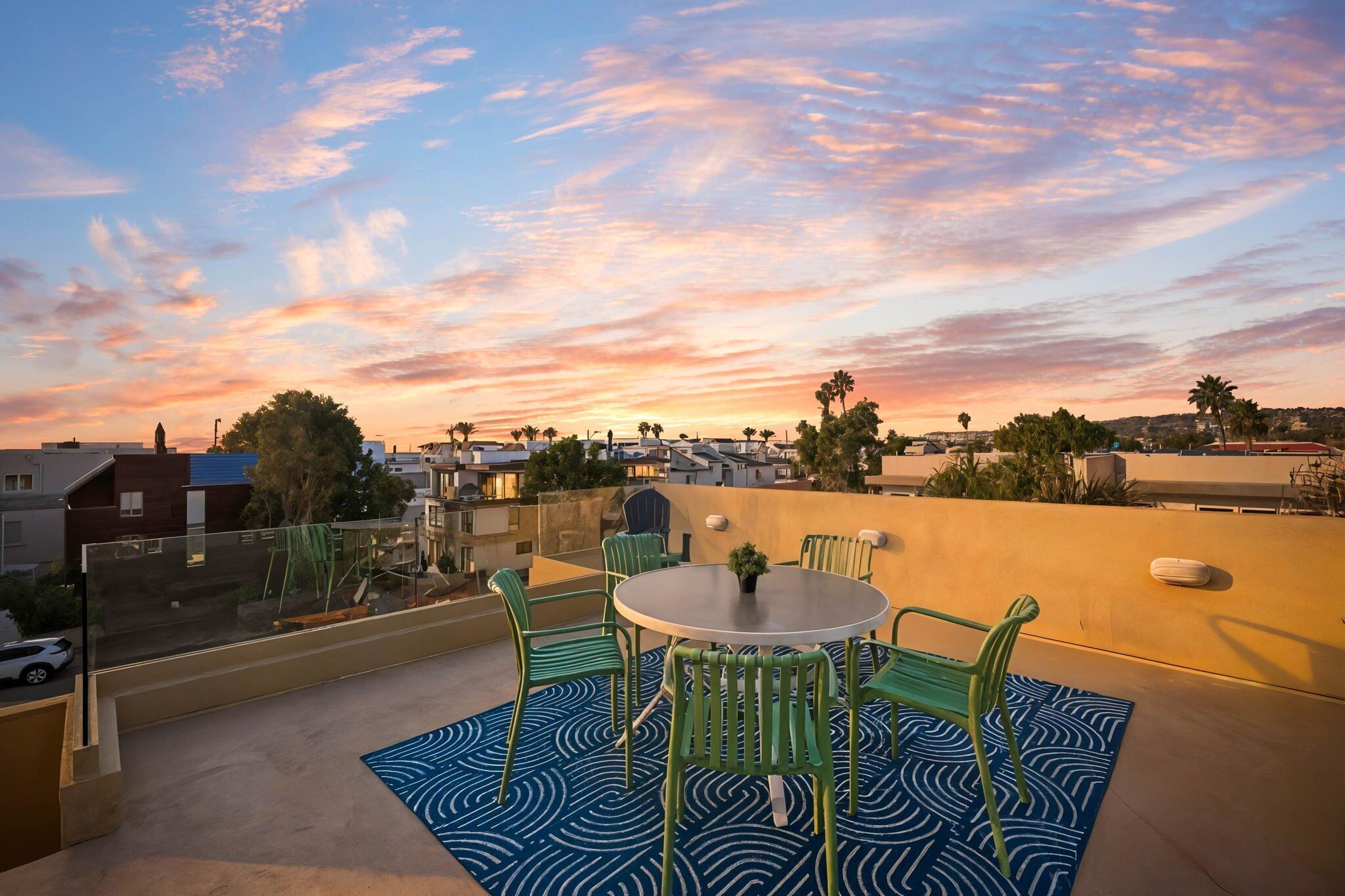 Une terrasse sur le toit, avec une table ronde et des chaises, un tapis à motifs et une vue sur le paysage urbain au coucher du soleil.