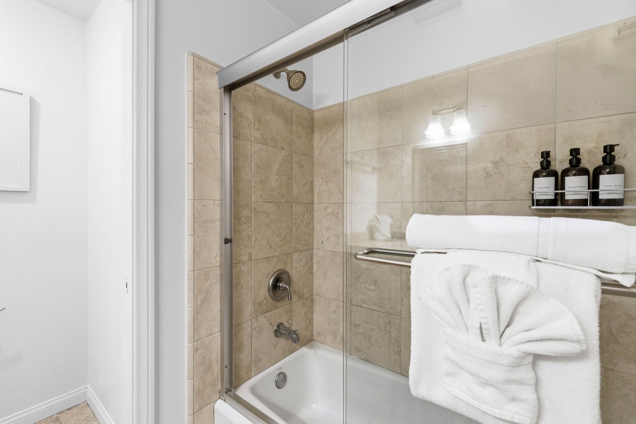 Un baño moderno con ducha de vidrio, una bañera blanca y un estante con artículos de aseo.