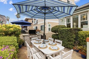 An outdoor patio with a grill, dining table set with plates, and striped umbrellas.
