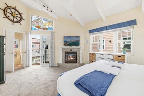 A bedroom with a bed, a fireplace, a TV, and a view of the outside.