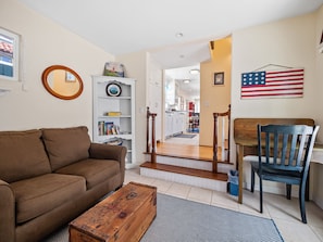 Cozy living room with a sofa, coffee table, bookshelf, and framed picture, featuring a staircase leading to an adjacent room.