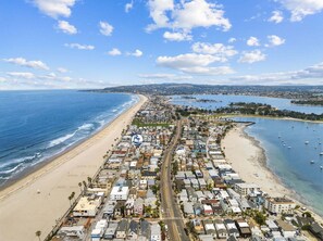 An aerial view of a coastal town with a beach, marina, and dense residential area.