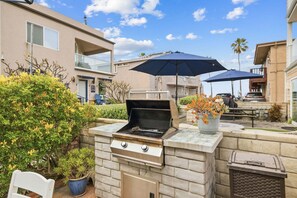 An outdoor grill area with a stone wall, potted plants, and umbrellas.