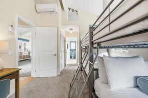 A bunk bed with a ladder, a white door, and a hallway leading to a bathroom.