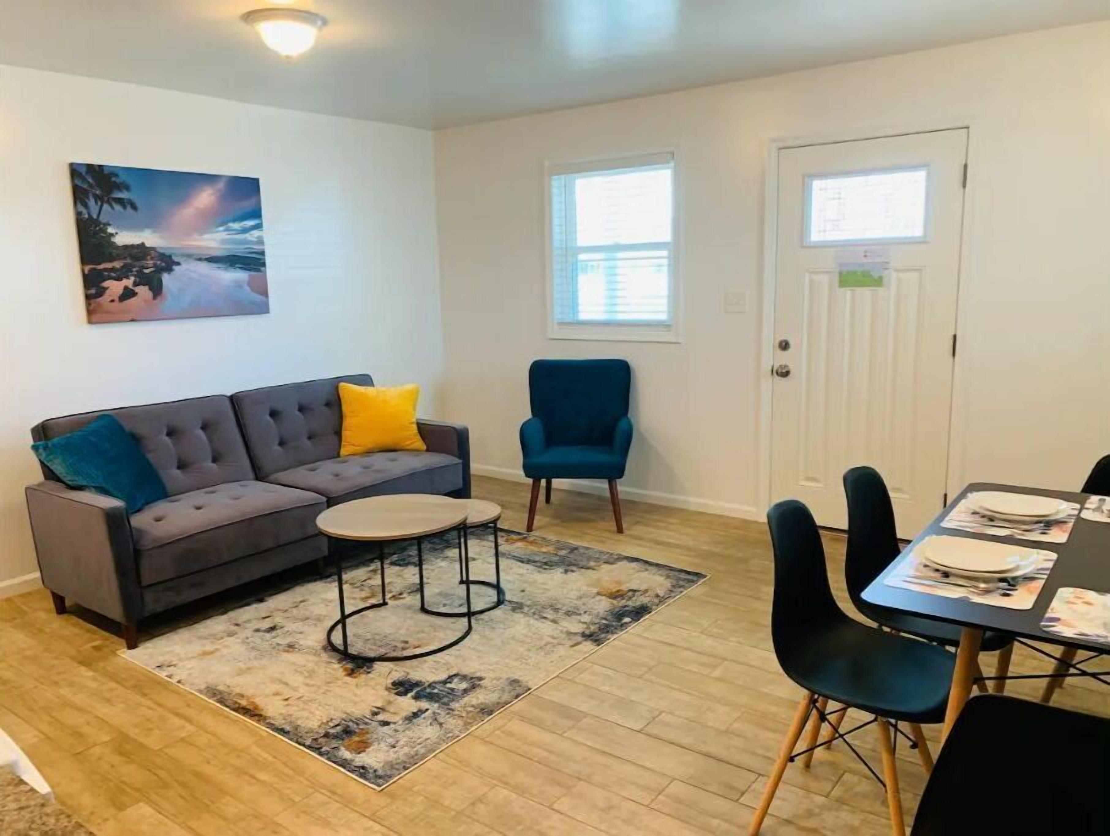 Un salon avec un canapé gris, un fauteuil bleu, une table basse et une table à manger dressée pour quatre personnes.