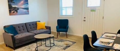 Un salon avec un canapé gris, un fauteuil bleu, une table basse et une table à manger dressée pour quatre personnes.