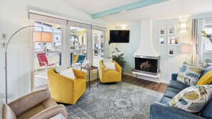 A living room with a fireplace, yellow armchairs, a blue sofa, and a large window overlooking a balcony. - All Day Bay Dream by Ryson Vacation Rentals (Galveston)