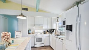 A modern kitchen with white cabinets, a stainless steel refrigerator, a built-in oven, and a large island with a sink. - All Day Bay Dream by Ryson Vacation Rentals (Galveston)