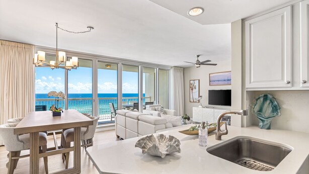Una cocina moderna con una isla grande, un comedor con vista al océano y una sala de estar con sofá y televisor.