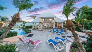 A resort pool area with lounge chairs, a gazebo, and a view of the sea.