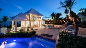 A pool area with a gazebo, lounge chairs, and a well-lit patio.