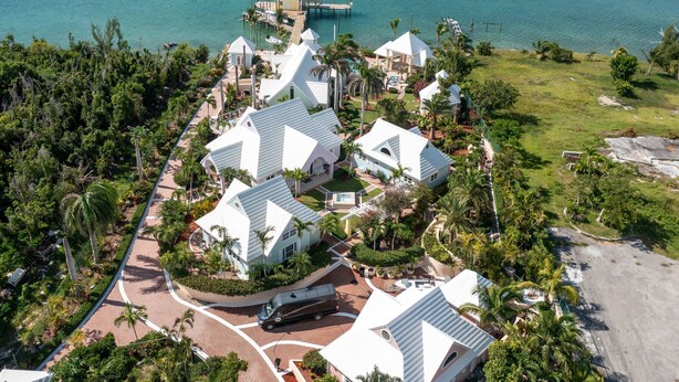 An aerial view of a resort with multiple white-roofed buildings, a dock, and a beach.