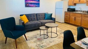 En kompakt opholdsstue med sofa, lille rundt bord og spiseplads.