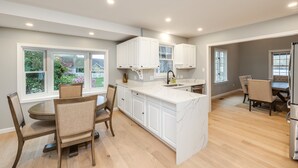 Una cocina moderna con armarios blancos, una isla de mármol y un comedor con sillas de madera.