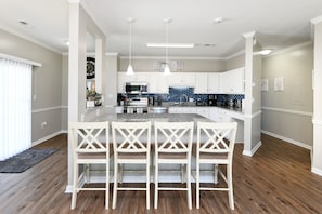 A modern kitchen with white cabinets, a granite countertop, and a central island with bar stools. - Beautiful Villa in Myrtle Beach within 4 min walk to the beach (Myrtle Beach)