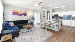 A modern living room with a sofa, coffee table, and a dining area with chairs. There is a kitchen with white cabinets and a microwave. - Beautiful Villa in Myrtle Beach within 4 min walk to the beach (Myrtle Beach)