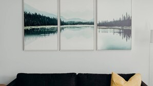A wall with three framed landscape paintings depicting serene lakes and forests.