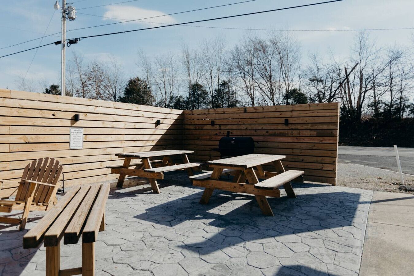 A picnic area with wooden benches and tables, a grill, and a wooden fence.