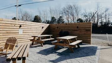 A picnic area with wooden benches and tables, a grill, and a wooden fence.