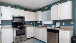 Une cuisine avec des meubles blancs, des appareils en acier inoxydable, une horloge et un panneau décoratif portant l’inscription « SEASHORE » au mur.
