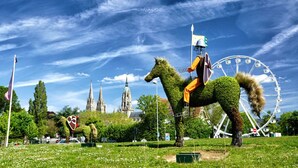 Una estatua de un caballo en un parque, con una noria y una iglesia al fondo.