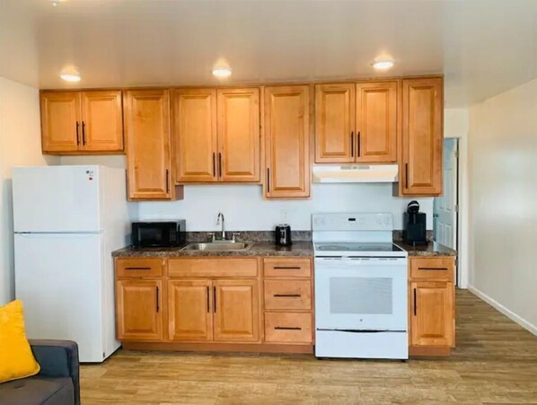 Compact kitchen with microwave, stainless steel sink, and white stove.