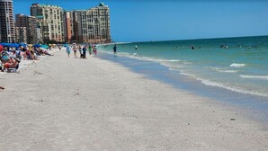 Una playa con gente y edificios al fondo.