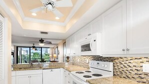 Una cocina moderna con armarios blancos, encimera de granito, estufa y microondas.