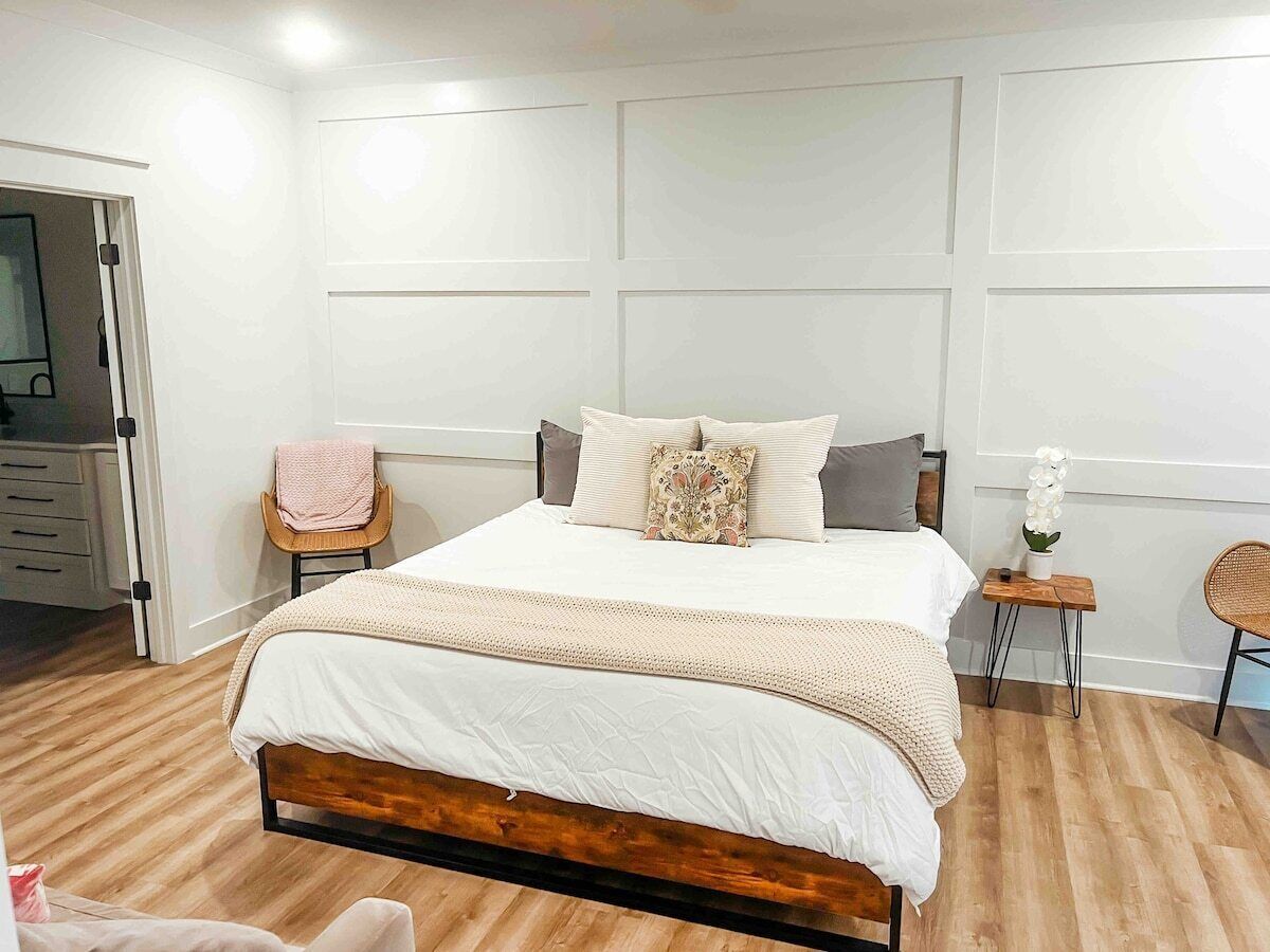 Una camera da letto con un letto in legno, biancheria bianca, un comodino con una pianta e una sedia.