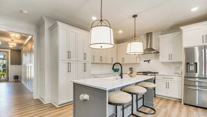 A modern kitchen with white cabinets, a central island with stools, stainless steel appliances, and pendant lighting.