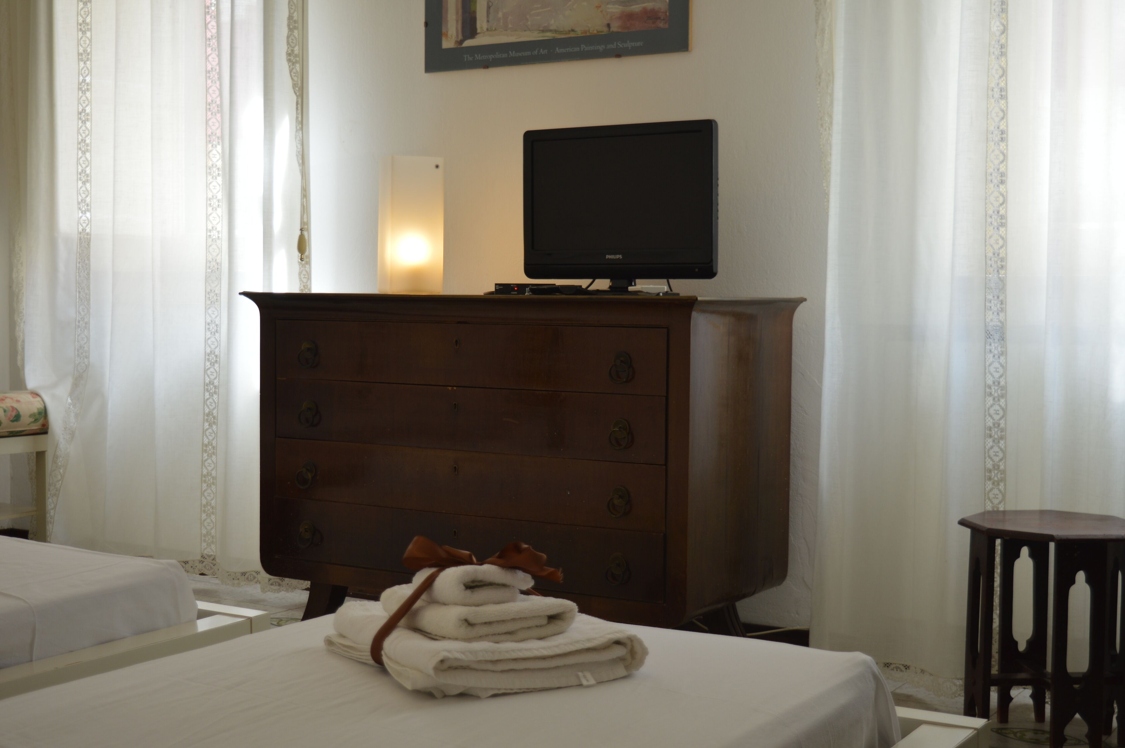A hotel room with a bed, a wooden dresser, a television on top of the dresser, and a small table.