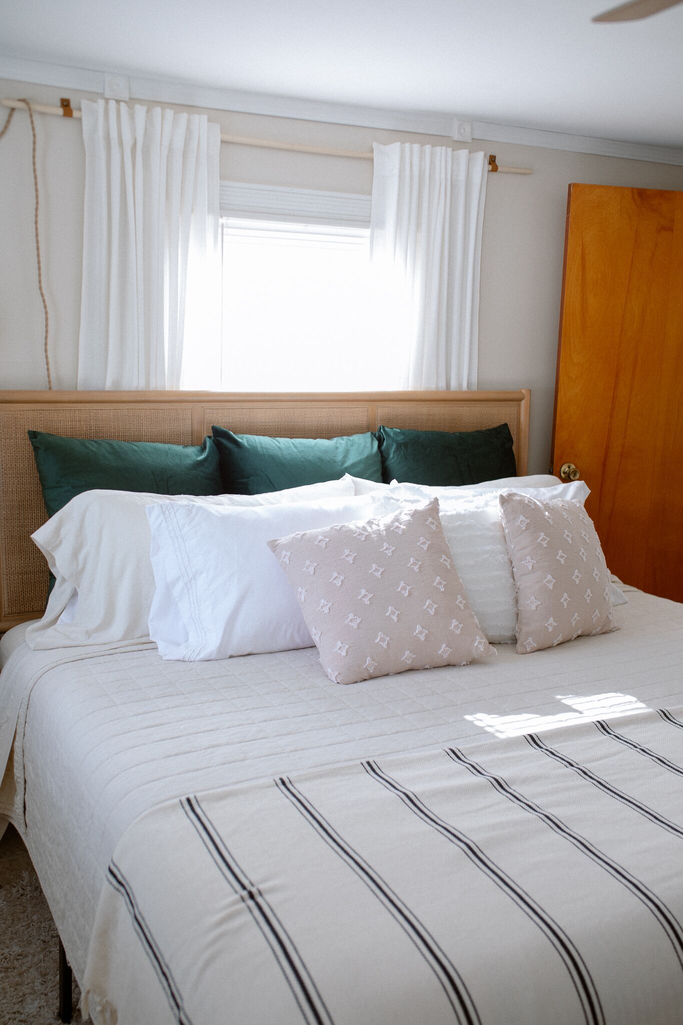 A neatly made bed with white and striped bedding, green and white pillows, and a wooden headboard.