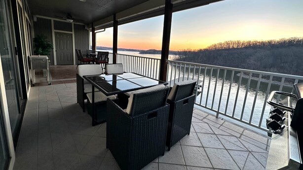 A balcony with a table and chairs, a ceiling fan, and a view of a river at sunset. - The Pointe at Lazy Days (Osage Beach)