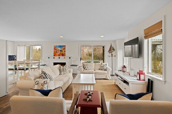 A spacious living room with a fireplace, white furniture, and large windows.
