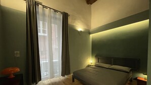 Et soveværelse med en seng, et natbord, en lampe og et vindue med gardiner.