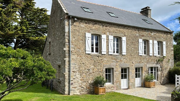 A stone building with a sloped roof, white shutters, and a sign reading "LAPOMMERAYE".