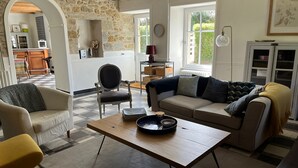 A cozy living room with a stone wall, a sofa, a coffee table, and a view of the kitchen and garden.