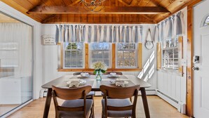 A dining area with a wooden ceiling, a chandelier, and a table set for four. - Outdoor Cape Cod Oasis just 5 minutes to S Village Beach! (Dennis)