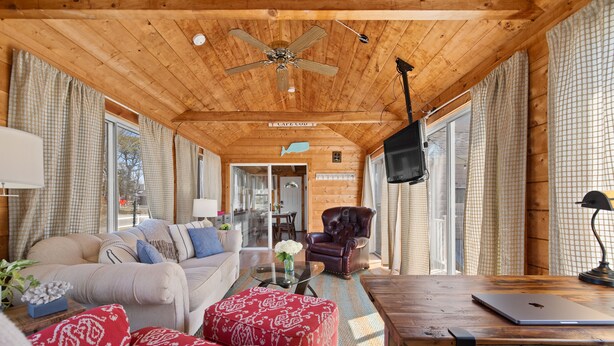 A cozy wooden interior with a sofa, ottoman, and a dining area. - Outdoor Cape Cod Oasis just 5 minutes to S Village Beach! (Dennis)